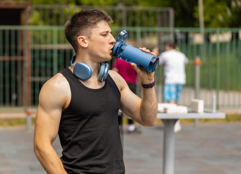 Dehydrated thirsty athletic runner muscular man in t-shirt drinking water from bottle after jogging