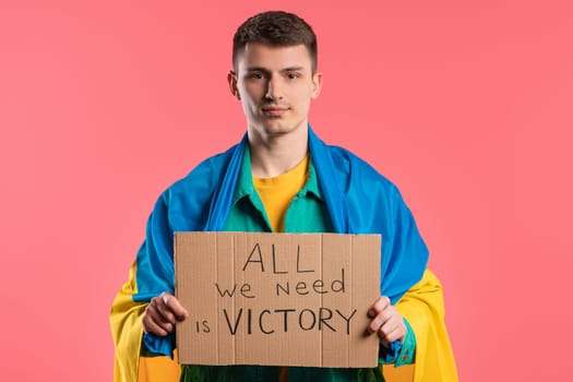 Ukrainian man with cardboard All we need is victory on pink background.