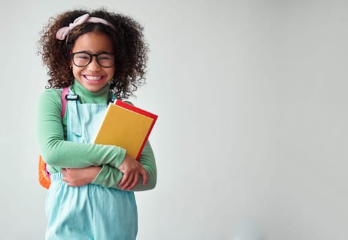 School, portrait of child student with books for knowledge, education and studying in a studio. Happy, smile and young smart girl kid with glasses for reading by a white background with mockup space.