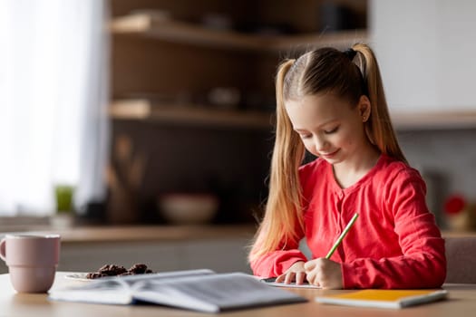 Cute Little Girl Writing In Notepad While Sitting At Desk At Home