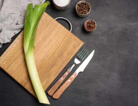 Leek on a wooden board, black table, top view