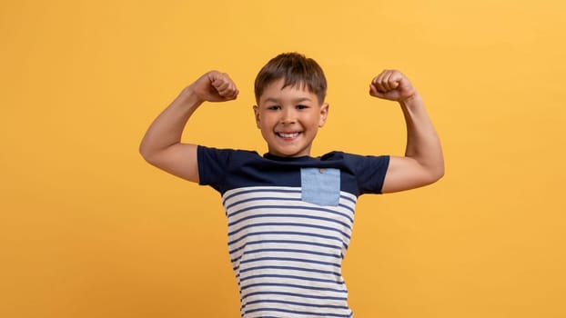 Funny cute boy showing his strong hands, yellow background