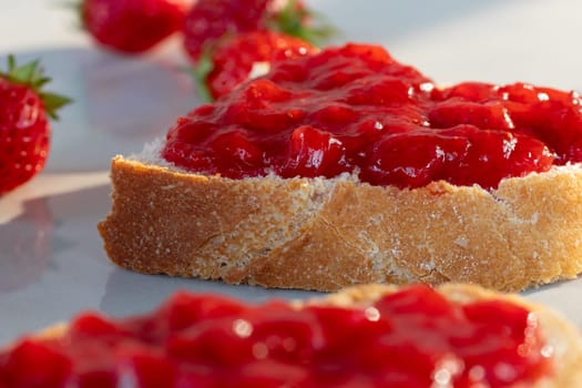 Wheat bread toasts with spread strawberry jam on the table, closeup