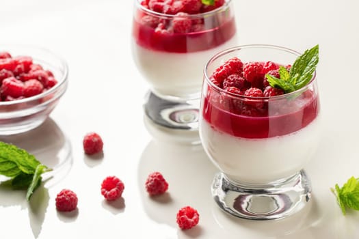 Panna cotta with raspberry jelly and mint leaves in glass glasses on a white table