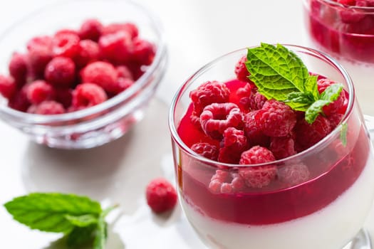 Panna cotta with raspberry jelly and mint leaves in glass glasses on a white table, close up