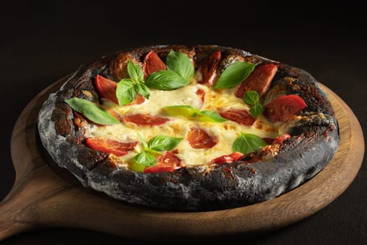 Black pizza margarita with tomatoes, mozzarella and basil. Dough with healthy bamboo charcoal powder