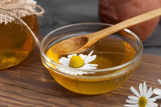 Chamomile syrup in a small bowl and in a jar on a wooden table