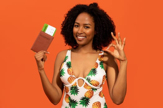 Attractive african lady in swimming clothes showing passport, tickets, okay