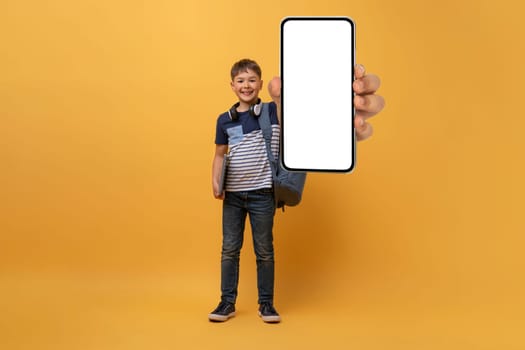 Happy child schoolboy showing smartphone with mockup, yellow background