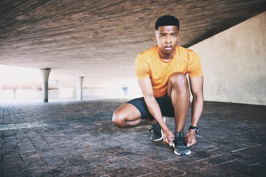 Discipline is the price of progress. a young man tying his shoelaces during a workout against an urban background.