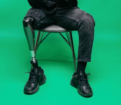 Cropped view of disabled young man with prosthetic leg, artificial limb concept. Studio shooting on green background