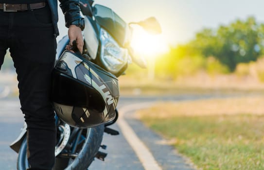 Motorcyclist holding safety helmet next to his motorbike near the road. Unrecognizable biker holding helmet next to motorbike near the road. Motorcycle safety helmet concept