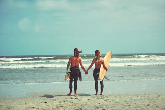 Relationship Goals. a young couple walking on the beach with their surfboards.