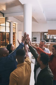Team spirit is knowing and living the belief that what a group of people can accomplish. a team high fiving each other in a office.