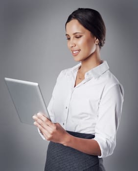 Researching consumer trends online. Studio shot of a young businesswoman using a digital tablet against a gray background.