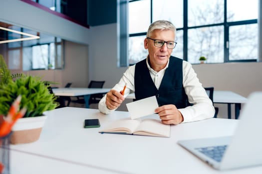 Busy senior man sitting at office desk with papers and making notes