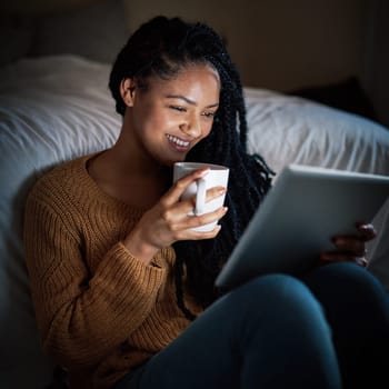 Indulging in some laziness after a long day. a relaxed young woman drinking coffee and using a digital tablet during the evening at home.