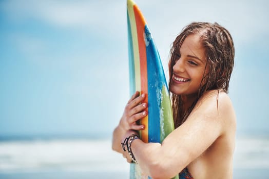 Board, were going to rip up those waves. an attractive young woman standing on a beach hugging her surfboard.