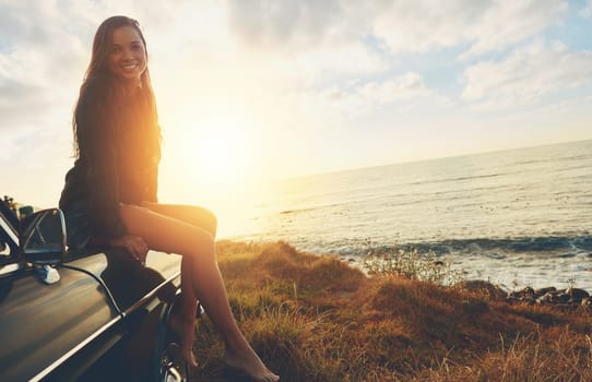 Road trip, portrait and sunset with a woman at the ocean, sitting on her car bonnet during travel for freedom or escape. Nature, flare and mockup with a young female tourist traveling in summer