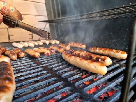 Delicious german sausages sizzling over the coals on barbecue grill.Man cooking meat on barbecue grill at bbq party in summer garden. Food, people and family time concept.appetizing sausages