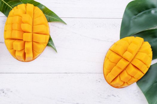 Beautiful chopped ripe mango with green leaves on bright white color wooden background, top view, flat lay, copy space. Tropical fruit design concept.