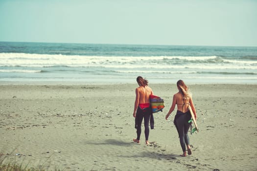 Everyday should be an adventure. a young couple walking on the beach with their surfboards.