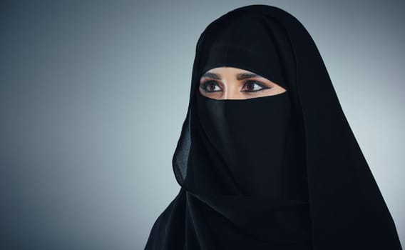 Drawing the veil over her beauty. Studio shot of a young muslim businesswoman against a grey background.