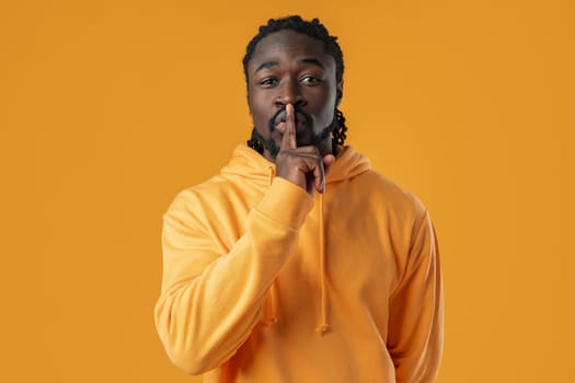 African man standing over yellow background showing silence gesture