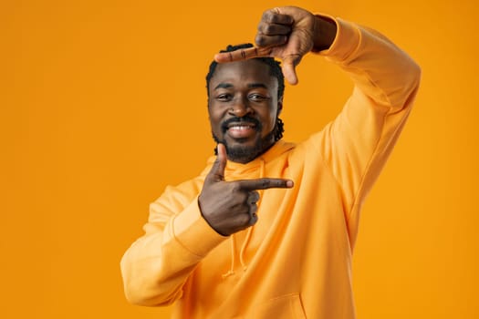 African man framing photograph with hands over yellow background.