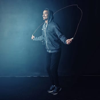 Its an all-body workout. Studio shot of a young man skipping against a dark background.