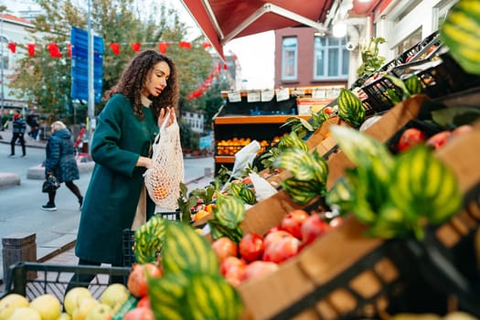 Young woman consumer choosing products to buy from local farmers market stand