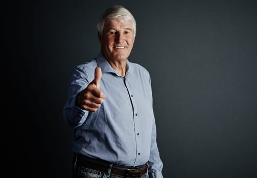 Feeling positive. Studio portrait of a handsome mature man giving you an approving thumbs up against a dark background.