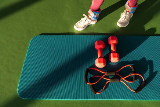 Woman legs near mat with expander and dumbbells