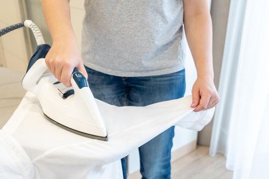 Woman ironing sleeve of white shirt with much steam