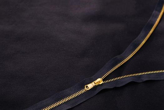 Background with open golden zipper on black fabric