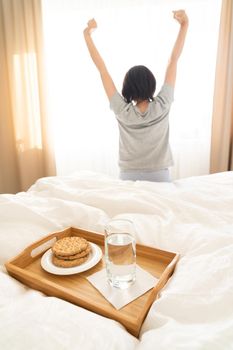Tray with water and crackers breakfast on a bed with woman stretching on background