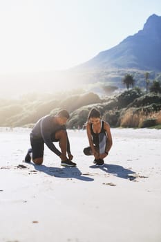 Lace up and lets get running. a sporty young couple tying their shoelaces while out for a run along the beach.