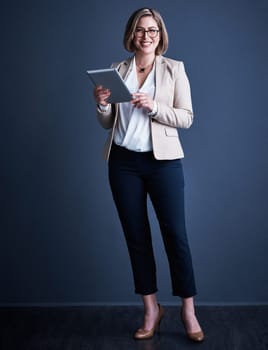 My dreams are within reach. Studio portrait of an attractive young corporate businesswoman using a tablet against a dark background.