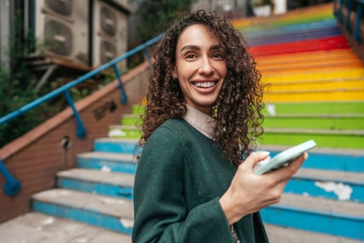 Young attractive woman stands near the rainbow stairs in Istanbul and using a phone