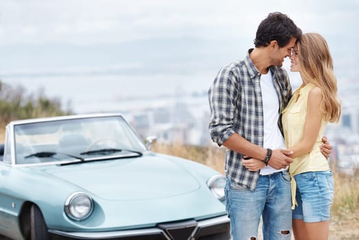 Stealing a kiss. A romantic young couple standing alongside their convertible while on a roadtrip.