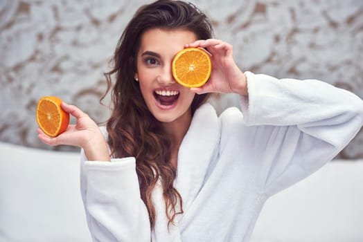 Orange, beauty and hide with woman in hotel for breakfast, diet and relax. Nutrition, health and natural with female model and cover face with citrus fruit in bedroom for vitamin c, spa and facial