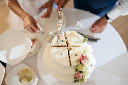 bride and a groom is cutting their stylish wedding cake on wedding banquet. Newlyweds holding knife and cutting together wedding cake