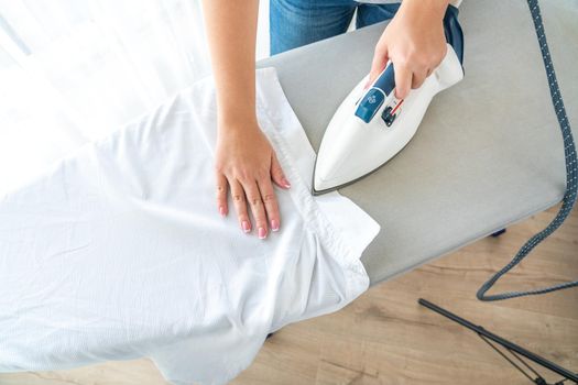 Top view of woman ironing white shirt collar on ironing board