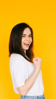 Victory Gesture: Enthusiastic Lady with Fist Raised in Triumph, Shouting in Excitement - Capturing Success, Achievement and Positive Energy Against a Yellow Background