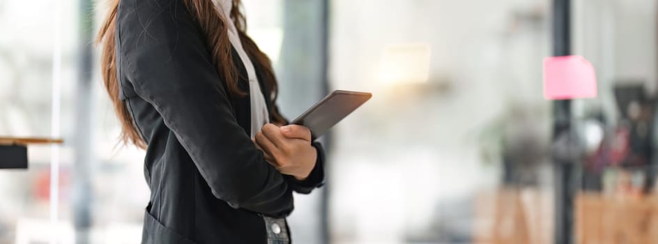 Close up young entrepreneur woman using her digital tablet while standing in office with copy space