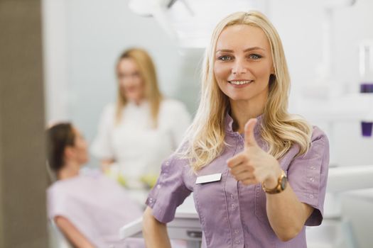 Portrait of a confident young woman standing with thumb up in a dentist’s office and looking at the camera.