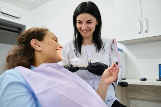 Smiling happy woman looking at her mirror reflection after teeth whitening procedure in dentistry clinic