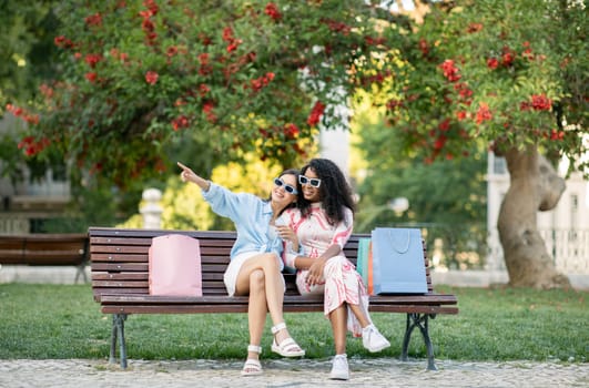 Two Happy Multiethnic Female Friends Relaxing On Bench After Shopping