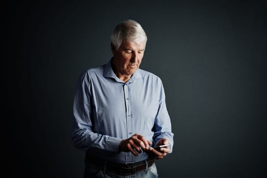 Sending a text message. Studio shot of a handsome mature man sending a text message against a dark background.
