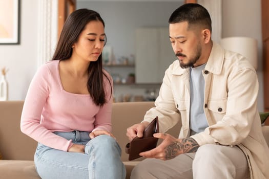 Unhappy Asian Couple Looking At Wallet Struggling Financial Issues Indoor